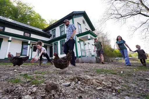 Soraya Holden, left, chases a chicken while walking with her family past their family home, Thursday, May 12, 2022, in Proctor, Vt. After fleeing one of the most destructive fires in California, the Holden family wanted to find a place that had not been so severely affected by climate change and chose Vermont. (AP Photo/Charles Krupa)