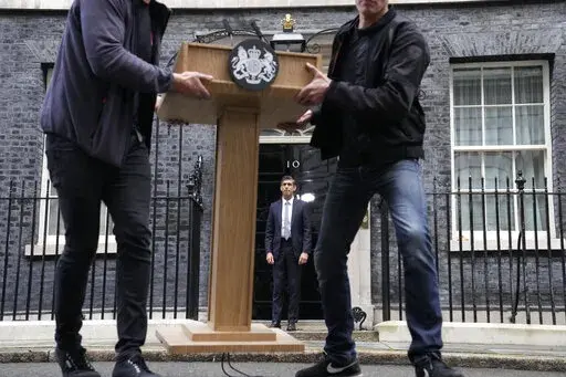New British Prime Minister Rishi Sunak, centre, poses for the media as the pulpit is moved after his speech at Downing Street in London, Tuesday, Oct. 25, 2022, after returning from Buckingham Palace where he was formally appointed to the post by Britain's King Charles III. In his first month as Britain's prime minister, Rishi Sunak has stabilized the economy, reassured allies from Washington to Kyiv and even soothed the European Union after years of sparring between Britain and the bloc. But Su