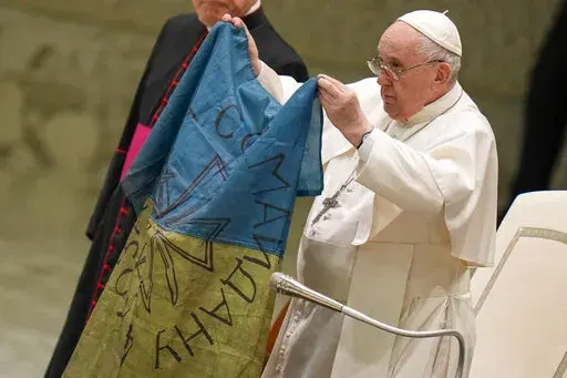 Pope Francis shows a flag that was brought to him from Bucha, Ukraine, during his weekly general audience in the Paul VI Hall, at the Vatican, Wednesday, April 6, 2022. (AP Photo/Alessandra Tarantino)