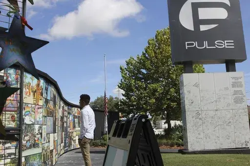 Brandon Wolf, a survivor of the Pulse nightclub shooting and activist, looks at the photos that are a part of the Pulse memorial in Orlando, Fla., on Sept. 9, 2022. Survivors, victims' families and residents of Orlando, had hoped by this time to have a permanent memorial in place for the eighth anniversary on Wednesday, June 12, 2024, of the Pulse nightclub massacre when 49 people were killed by a gunman at a club with an LGBTQ+ clientele on Latin night. (AP Photo/Cody Jackson, File)