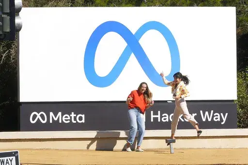 Facebook employees take a photo with the company's new name and logo outside its headquarters in Menlo Park, Calif., on Oct. 28, 2021.  Meta, the company that owns Facebook, Instagram and WhatsApp, saw its stock plunge after-hours Wednesday, Feb. 2, 2022, after reporting a rare decline in its fourth quarter profit due to a sharp increase in expenses. (AP Photo/Tony Avelar, File)
