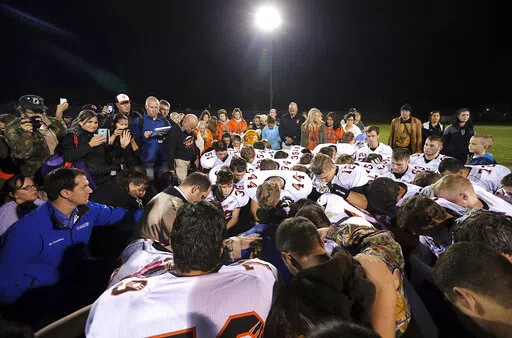 Bremerton assistant football coach Joe Kennedy, obscured at center in blue, is surrounded by Centralia High School football players as they kneel and pray with him on the field after their game against Bremerton on Oct. 16, 2015, in Bremerton, Wash. After losing his coaching job for refusing to stop kneeling in prayer with players and spectators on the field immediately after football games, Kennedy will take his arguments before the U.S. Supreme Court on Monday, April 25, 2022, saying the Breme