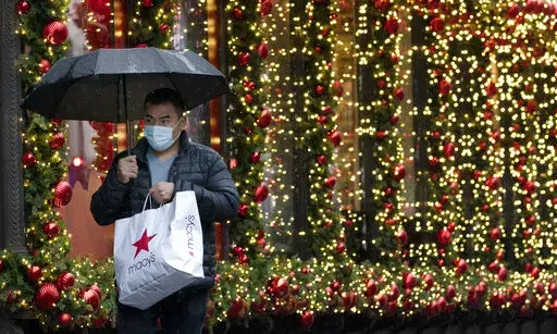 In this Nov. 30, 2020 file photo, a shopper walks by a holiday window display in New York. Financial educators are often working on overdrive during the holiday shopping season, dispensing advice to consumers about budgeting and staying out of debt. We asked five financial educators how they personally survive the holiday season with their finances intact. They shared some novel strategies, such as saving for the season starting in January and even buying gifts that early, giving nontraditional 