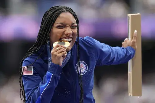Women's long jump gold medalist Tara Davis-Woodhall, of the United States, bites into her medal on the podium at the 2024 Summer Olympics, Friday, Aug. 9, 2024, in Saint-Denis, France. (AP Photo/Bernat Armangue)