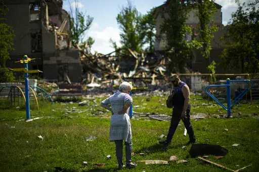Local residents stand next to a school destroyed in a Russian bombing in Bakhmut, eastern Ukraine, Tuesday, May 24, 2022. The town of Bakhmut has been coming under increasing artillery strikes, particularly over the last week, as Russian forces try to press forward to encircle the city of Sieverodonetsk to the northeast. (AP Photo/Francisco Seco)