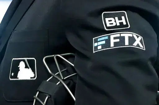 The FTX logo appears on a home plate umpire's jacket at a baseball game with the Minnesota Twins on Sept. 27, 2022, in Minneapolis. The imploding cryptocurrency trading firm FTX is now short billions of dollars after experiencing the crypto equivalent of a bank run. (AP Photo/Bruce Kluckhohn, File)