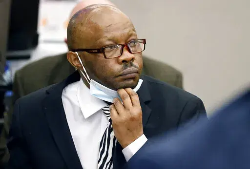 Defendant Billy Chemirmir lowers his mask as a state witness is asked to identify him during his murder trial at the Frank Crowley Courts Building in Dallas, Nov. 17, 2021. The retrial of the man charged with killing 18 older women in the Dallas area over a two-year span is set to begin Monday, April 25, 2022 after the first jury to hear a case against him deadlocked. Chemirmir faces life in prison without parole if he’s convicted of capital murder in the smothering of 81-year-old Lu Thi Harri