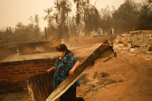 A woman clears debris from a landscape of charred remains in Santa Ana, Chile, Saturday, Feb. 4, 2023. At least 13 people were reported dead as a result of the wildfires burning across Chile that have destroyed homes and thousands of acres of forest while the South American country is in the midst of a heat wave. (AP Photo/Matias Delacroix)