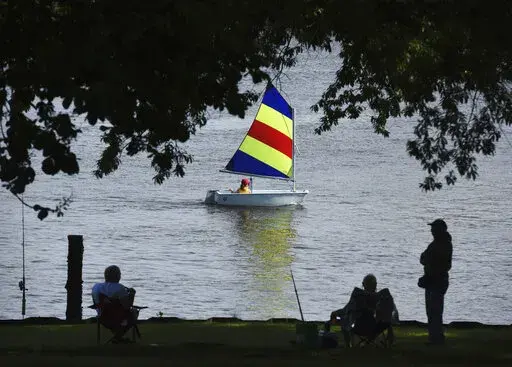 A sailor with the St. Joseph Junior Foundation Summer Sailling School cruises past fishermen along the St. Joseph River in St. Joseph, Mich., Wednesday, June 15, 2022.  The fast-changing coronavirus has kicked off summer in the U.S. with lots of infections but relatively few deaths compared to its prior incarnations. COVID-19 is still killing hundreds of Americans each day, but for many people the virus is not nearly as dangerous as it was.  (Don Campbell/The Herald-Palladium via AP)