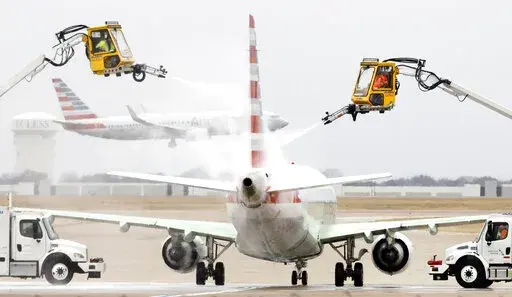 Aerial crews deice an American Airlines jet before it can take off as another lands at Dallas/Fort Worth International Airport, Wednesday, Feb. 23, 2022, in Dallas. Light precipitation was falling as temperatures were in the mid 20's. (Tom Fox/The Dallas Morning News via AP)