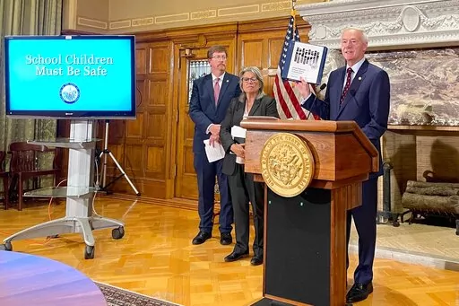 Arkansas Gov. Asa Hutchinson holds up an interim report from a commission formed to review school safety measures at a news conference at the state Capitol in Little Rock, Arkansas, on Tuesday, Aug. 2,2022. A proposed $50 million grant program for school safety is on the agenda for a legislative special session that is being held this week. (AP Photo/Andrew DeMillo)